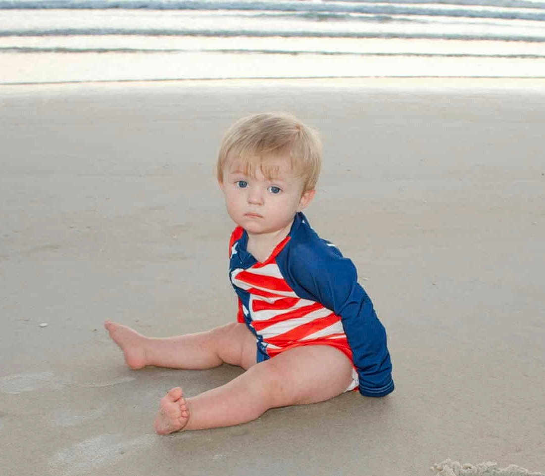 Westen is registered to the contest to win money with this photo: toddler, child, beach, sand, water, waves, swimsuit, red, white, blue, sitting, barefoot, serious, young_child, outdoor, summer, ocean, coast, nature, person