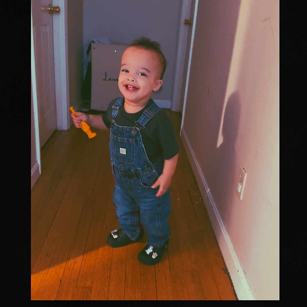 Jayden joined the competition — help win amazing prizes! toddler, child, smiling, hallway, wooden_floor, toy, shadow, denim_overalls, black_shirt, indoor, door, wall, happy, person, footwear, shadow_play, cute, young_child, standing, home
