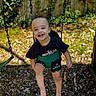 child, toddler, swing, outdoor, smile, happy, playground, sunlight, grass, petals, greenery, clothing, black_shirt, shorts, barefoot, fun, joy, face, person, leisure