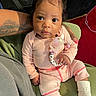 baby, infant, child, portrait, sitting, indoors, pink_outfit, bow, pacifier, teether, name_beads, socks, green_seat, car_seat, adult_arm, tattoo, close_up, wide_eyes, serious_expression, cozy
