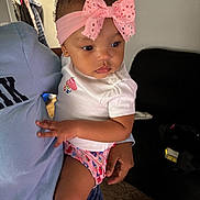 Gianna is registered to the contest to win money with this photo: toddler, child, baby, headband, pink_bow, white_shirt, cupcake_design, colorful_clothing, person, adult, holding, indoor, living_room, couch, carpet, hand, curly_hair, earrings, casual_clothing, home
