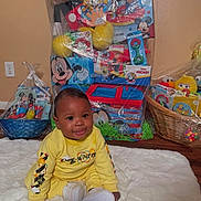 Jasani joined the competition — help win amazing prizes! baby, child, yellow_clothing, sitting, smiling, toy_baskets, mickey_mouse, sesame_street, gift_baskets, indoor, carpet, happy, cute, floor, white_rug, playful, colorful, wrapped_gifts, basket, home