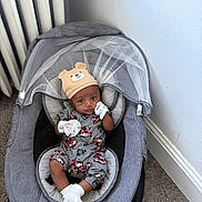Christopher joined the competition — help win amazing prizes! baby, infant, baby_rocker, hat, bear_hat, pajamas, white_socks, mesh_canopy, gray_fabric, carpet, radiator, corner, indoor, child, cute, looking_at_camera, seated, comfortable, home, cozy