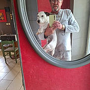 Phylou a rejoint le concours — aidez-le/la à gagner de superbes lots ! black_ears, casual, chair, dog, glasses, gray_shirt, holding, home, indoor, man, mirror, phone, portrait, red_wall, reflection, selfie, table, tiled_floor, white_dog, wooden_plaque