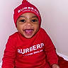 baby, child, smiling, red_clothing, hat, burberry, happy, portrait, indoors, sitting, infant, cute, fashion, apparel, person, headwear, joyful, studio, one_person, bright