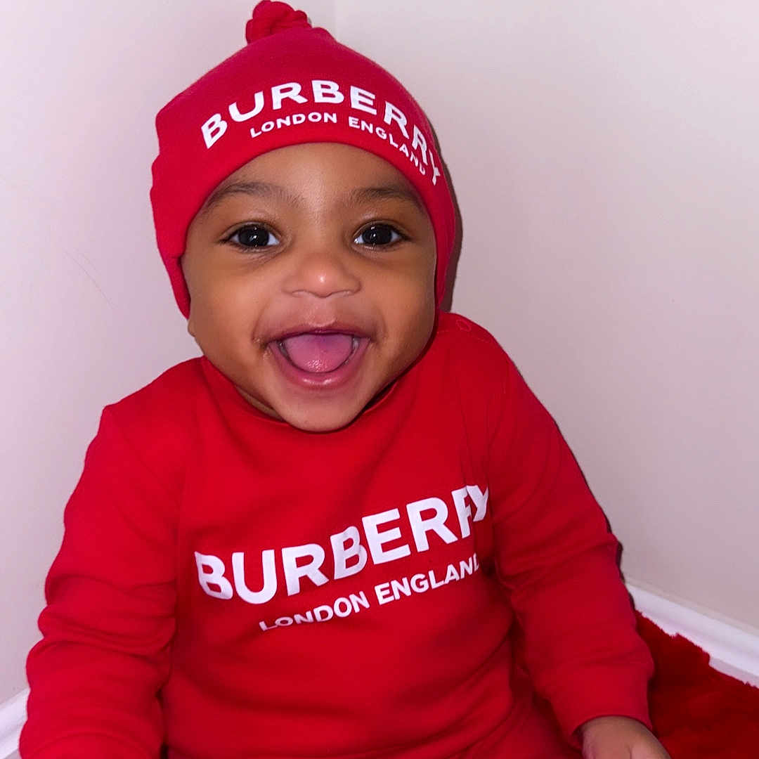 Naujourr is registered to the contest to win money with this photo: baby, child, smiling, red_clothing, hat, burberry, happy, portrait, indoors, sitting, infant, cute, fashion, apparel, person, headwear, joyful, studio, one_person, bright