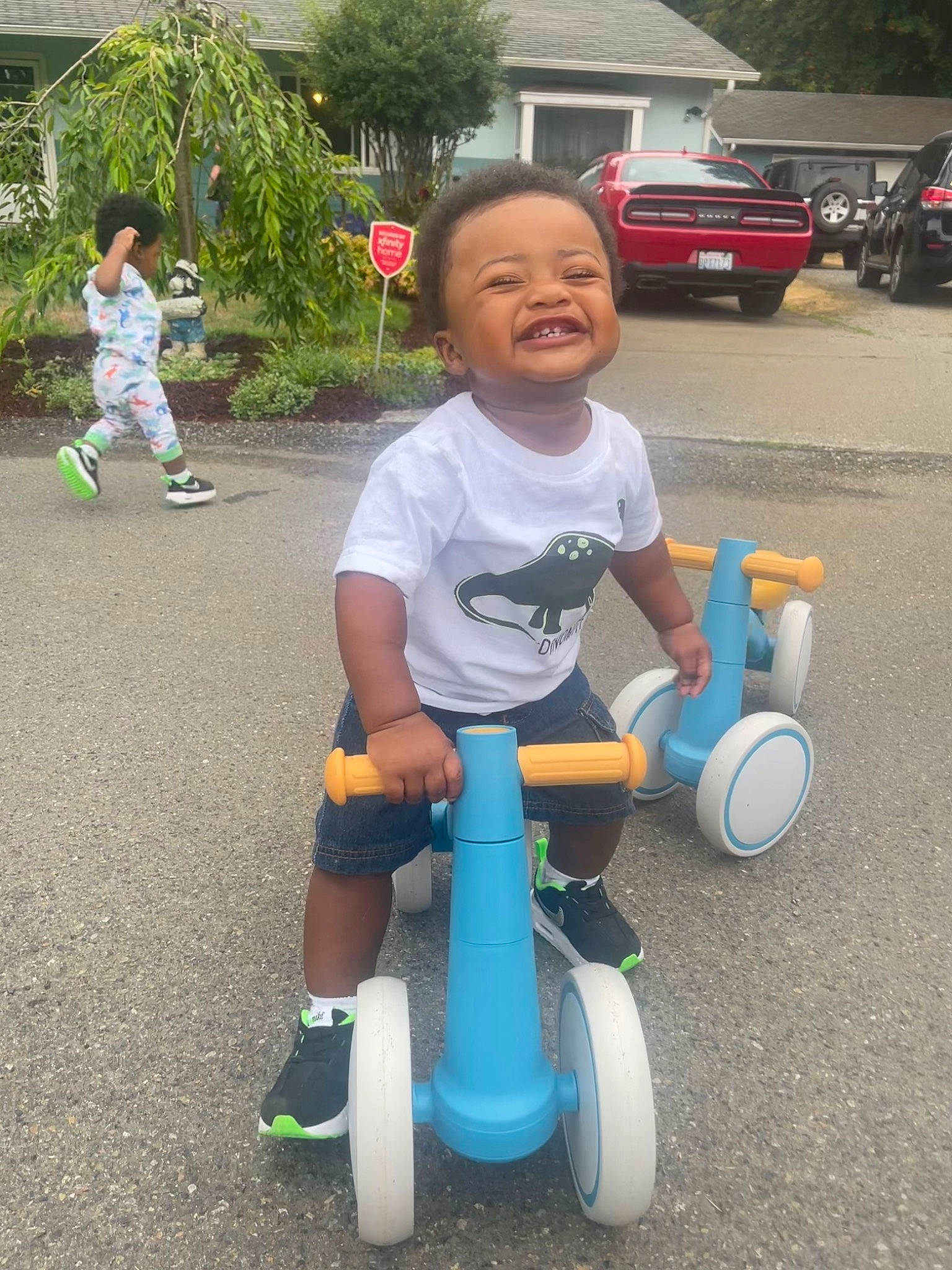 Kyrie is registered to the contest to win money with this photo: asphalt, automotive_tire, car, child, city, electric_blue, fun, grass, human_body, leisure, person, plant, play, recreation, riding_toy, smile, tire, toddler, tree, vehicle