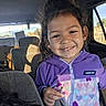 child, smiling, purple_jacket, heart_pattern, car_interior, seat, sunlight, shadow, young_girl, casual_clothing, happy, portrait, daylight, window, hair, person, childhood, cute, indoor, seated