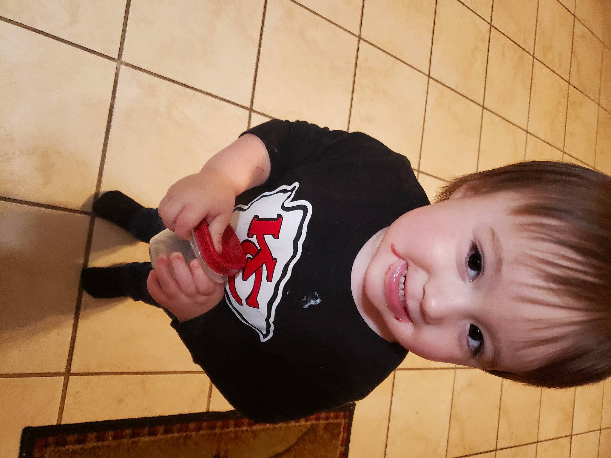 Lawrence is registered to the contest to win money with this photo: baby_toddler_clothing, carmine, cheek, elbow, floor, flooring, fun, gesture, happy, human_leg, joy, knee, nose, person, sleeve, smile, thigh, thumb, tile_flooring, toddler