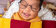 Mia Michelle is registered to the contest to win money with this photo: baby, glasses, blanket, smile, tongue, face, child, cute, portrait, wrapped, cozy, warm, soft, happy, infant, young_child, head, lying_down, colorful, texture