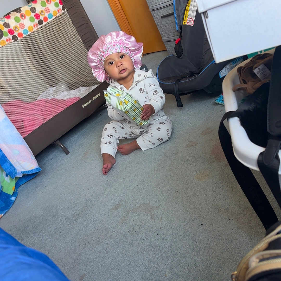 Emmah joined the competition — help win amazing prizes! baby, bonnet, car_seat, carpet, child, cute, door, drawer, floor, furniture, holding, indoor, infant, pajamas, person, playpen, room, sitting, snack, toy