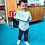 Logan a rejoint le concours — aidez-le/la à gagner de superbes lots ! child, boy, whiteboard, classroom, carpet, furniture, smiling, standing, indoor, clothing, shoes, writing, person, education, school, desk, shelf, background, happy, young