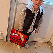 Logan a rejoint le concours — aidez-le/la à gagner de superbes lots ! child, boy, indoor, standing, school_bag, red, denim_vest, hoodie, sneakers, door, frosted_glass, tile_floor, curious, spiky_hair, casual_clothing, portrait, young, holding, looking_at_camera, home