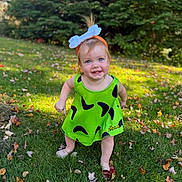 Dani is registered to the contest to win money with this photo: baby, child, toddler, smiling, happy, outdoors, autumn, leaves, grass, garden, costume, green_dress, blue_bow, headband, portrait, standing, sunlight, trees, fall, halloween