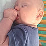baby, sleeping, thumb_sucking, onesie, blue_clothing, infant, face, ear, hand, arm, crib, wooden_bars, soft_surface, closeup, peaceful, cute, child, indoors, portrait, resting