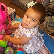 Athena joined the competition — help win amazing prizes! baby, blanket, child, colorful, curious, dress, floor, flower, girl, hair_accessory, household, indoor, person, plastic_eggs, playpen, playtime, seated, soft_surface, toy, young_child
