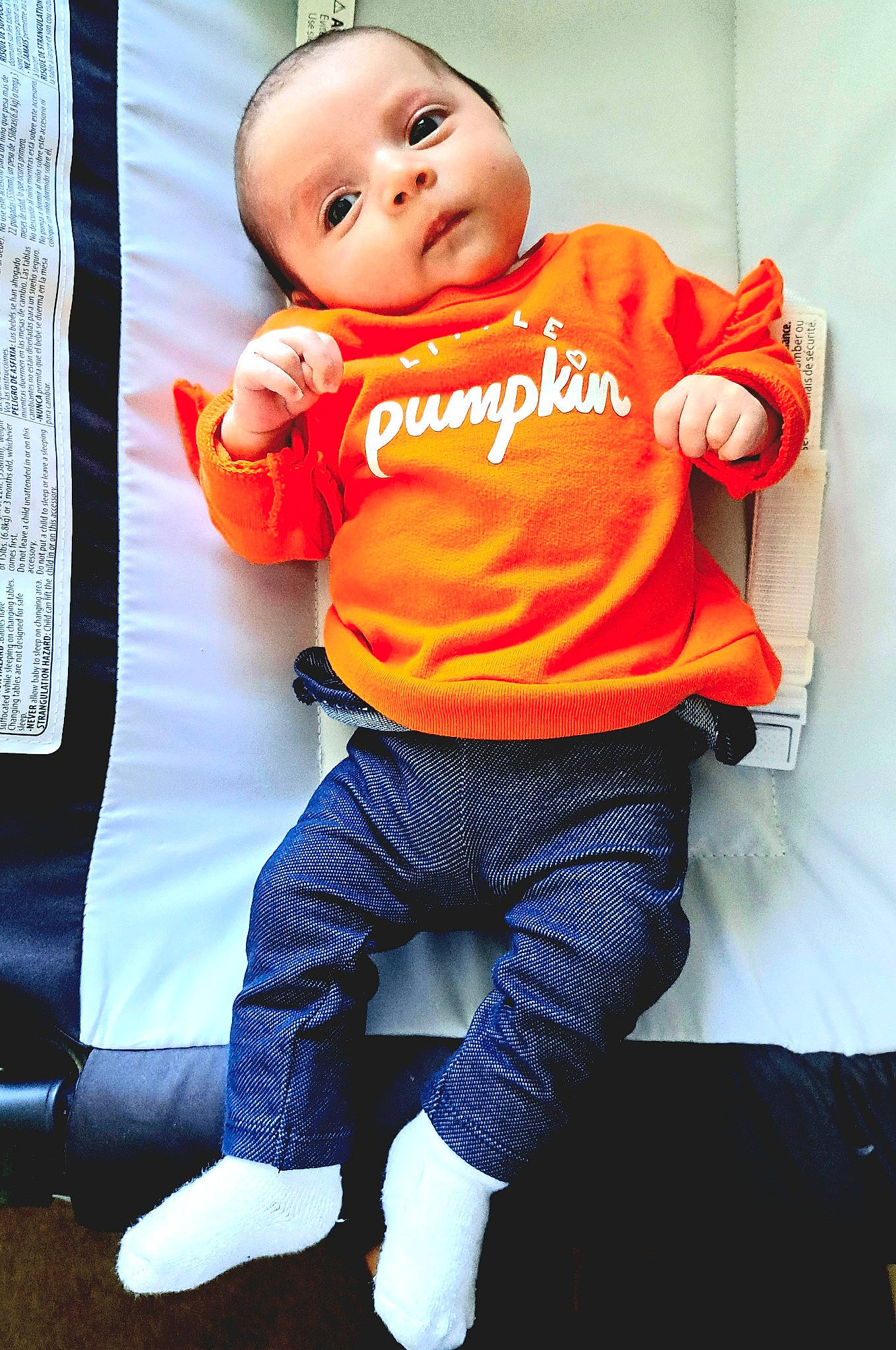 Harley is registered to the contest to win money with this photo: baby, baby_toddler_clothing, child, electric_blue, eye, face, happy, head, jersey, knee, orange, pattern, person, personal_protective_equipment, sleeve, sock, sportswear, t_shirt, textile, thigh