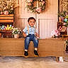 toddler, child, boy, sitting, blue_shirt, suspenders, jeans, black_shoes, easter_eggs, flower_wreath, wooden_crates, flowers, pastel_colors, rustic, bench, indoor, decor, spring, cute, portrait
