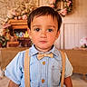 child, boy, portrait, face, clothing, bow_tie, suspenders, shirt, indoors, decor, flowers, wooden_crates, background, cute, young, person, expression, colorful, warm, casual