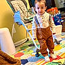 child, toddler, indoor, playmat, high_chair, suspenders, sneakers, clothing, floor, colorful, toy, person, home, furniture, young_child, portrait, standing, cute, casual, room