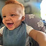 baby, smiling, high_chair, bib, red_hair, happy, child, indoor, portrait, cute, face, expression, toddler, clothing, person, seat, fun, joy, infant, reaching
