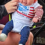 baby, child, blue_bow, headband, shirt, patriotic, american_flag, hand, legs, socks, stroller, outdoor, grass, person, celebration, smiling, cute, infant, clothing, summer