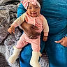 baby, child, infant, pink_bow, smiling, person, adult_hand, blue_pants, blanket, cozy, indoor, home, soft_texture, clothing, socks, cute, happy, seated, portrait, holding