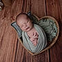 newborn, baby, sleeping, wrapped, blanket, heart_shaped_bowl, wooden_floor, cozy, peaceful, infant, soft, pillow, dried_leaves, natural, portrait, indoors, calm, hands, tiny, cute