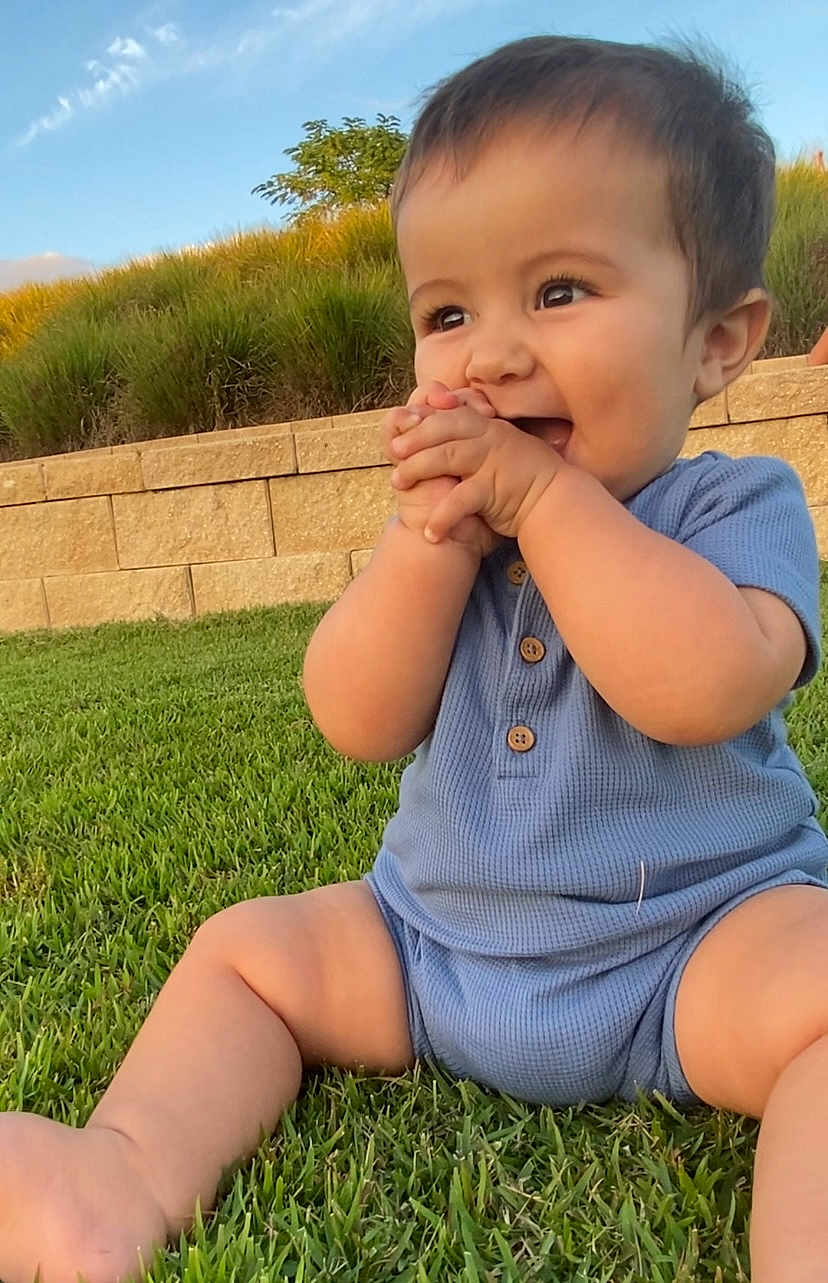 Maverick joined the competition — help win amazing prizes! baby, child, smiling, grass, outdoor, blue_clothing, happy, sitting, hands, face, nature, sunlight, greenery, garden, cute, portrait, infant, young_child, daylight, skin