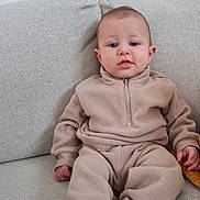 Adam participe au concours pour gagner de l'argent avec cette photo : baby, child, fleece, beige, couch, sitting, socks, cozy, indoor, portrait, young_child, casual_clothing, furniture, person, cute, relaxed, looking_at_camera, home, infant, neutral_colors