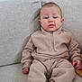 baby, child, fleece, beige, couch, sitting, socks, cozy, indoor, portrait, young_child, casual_clothing, furniture, person, cute, relaxed, looking_at_camera, home, infant, neutral_colors