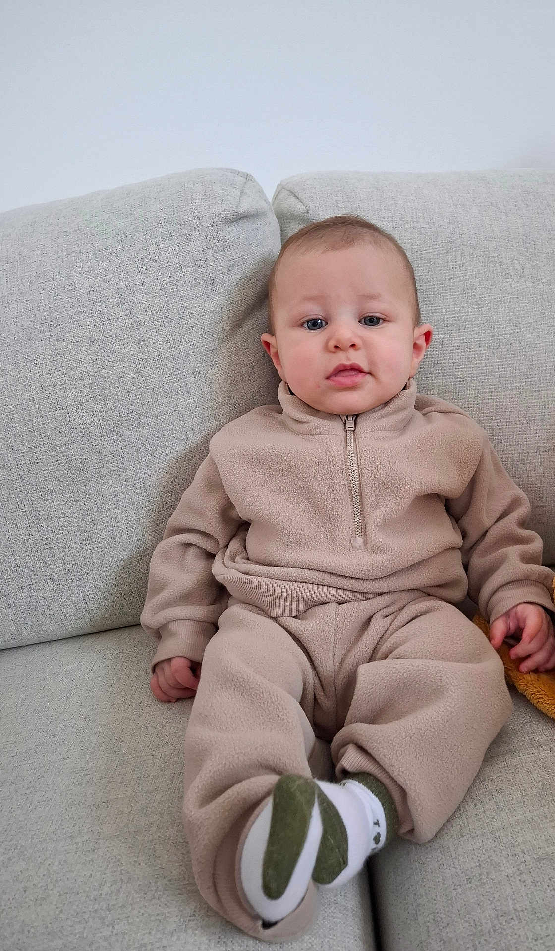 Adam participe au concours pour gagner de l'argent avec cette photo : baby, child, fleece, beige, couch, sitting, socks, cozy, indoor, portrait, young_child, casual_clothing, furniture, person, cute, relaxed, looking_at_camera, home, infant, neutral_colors