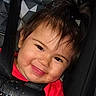 toddler, child, smiling, face, hair, pony_tail, car_seat, seat_belt, clothing, red_shirt, happy, close_up, baby, cute, indoors, portrait, skin, eyes, mouth, cheeks