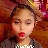 Roselynn is registered to the contest to win money with this photo: child, face, red_lipstick, indoor, wooden_wall, necklace, tshirt, portrait, young, person, expression, text_overlay, timestamp, casual, brown_hair, lighting, warm_tone, fashion, closeup, sitting
