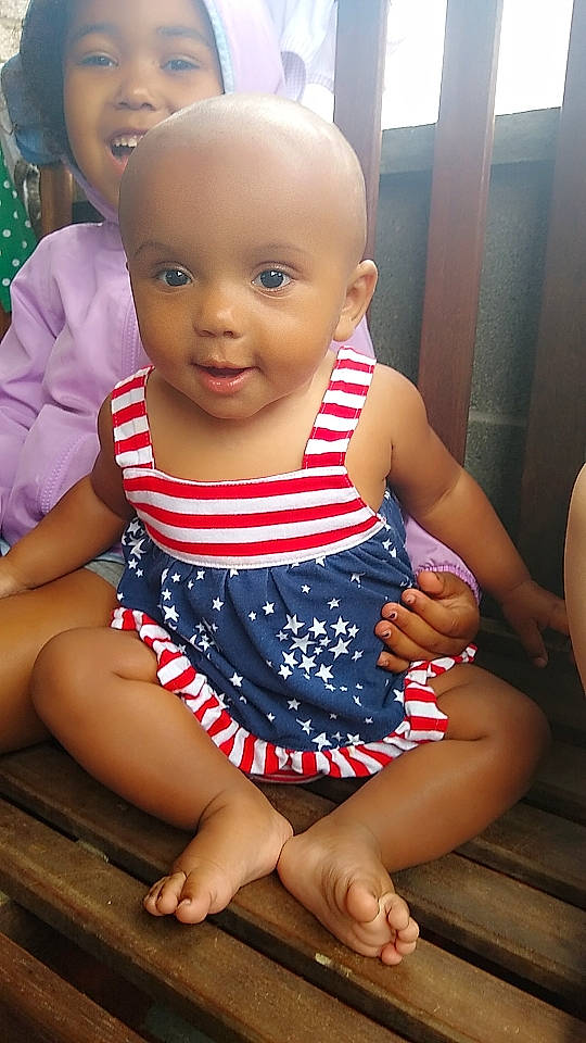 Ella is registered to the contest to win money with this photo: baby, baby_toddler_clothing, cheek, child, day_dress, finger, fun, hairstyle, happy, joint, leisure, one_piece_garment, pattern, person, pink, sitting, skin, sleeve, smile, thigh