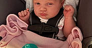 Rosalyn is registered to the contest to win money with this photo: baby, infant, car_seat, blanket, pacifier, pink, clothing, face, person, child, newborn, resting, indoors, seatbelt, cute, small_hands, portrait, expression, sleepy, cozy