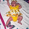 baby, infant, smiling, yellow_dress, headband, blanket, floral_pattern, butterfly, happy, lying_down, cute, child, portrait, colorful, indoors, small_person, playful, cheerful, clothing, fabric