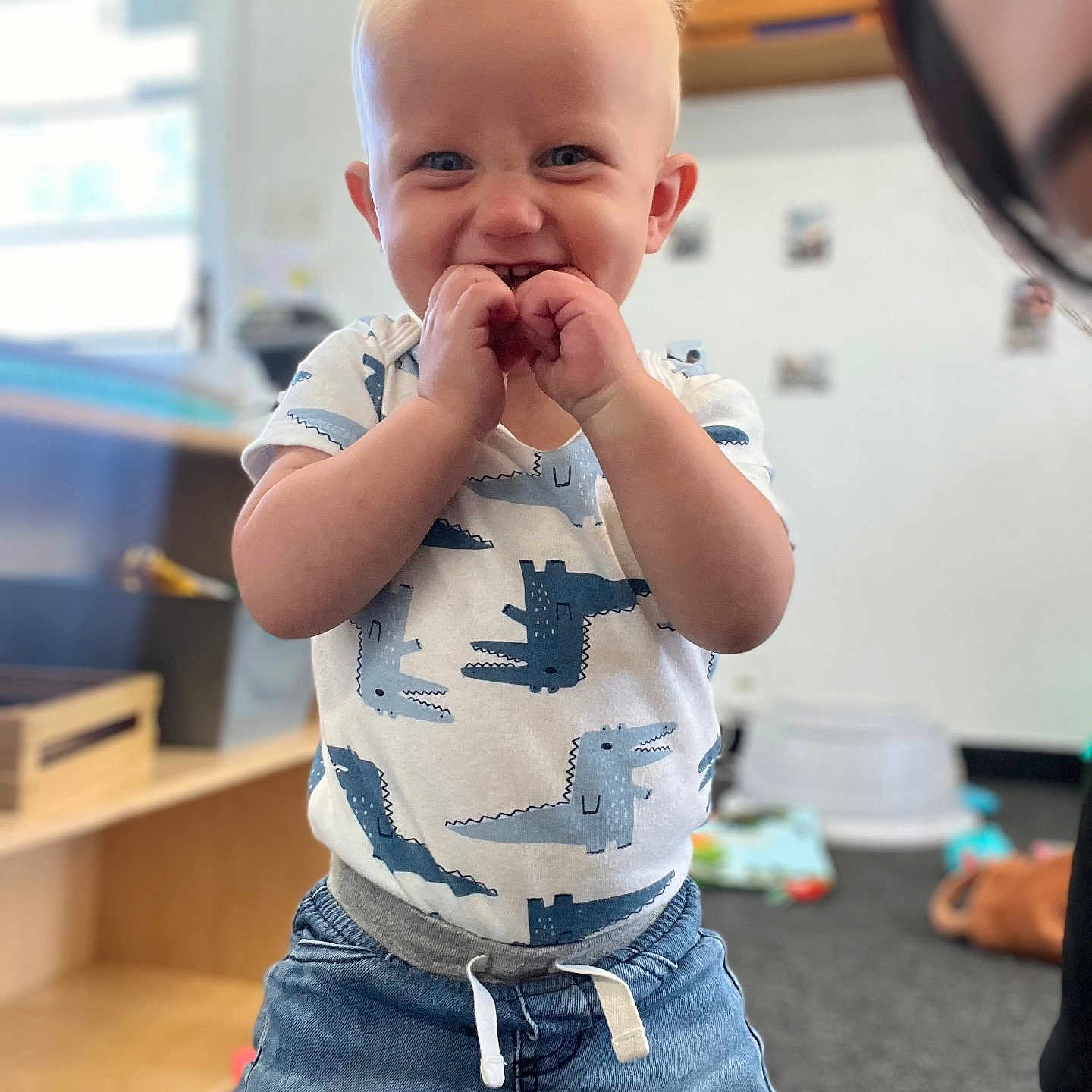 Hendrix is registered to the contest to win money with this photo: blond_hair, blue_eyes, carpet, child, clothing, cute, denim_pants, dinosaur_print, furniture, happy, indoor, person, playroom, portrait, shirt, smiling, standing, toddler, toy, young_child