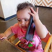 Lahlani joined the competition — help win amazing prizes! child, toddler, baby, high_chair, smartphone, phone_case, pink_shirt, strawberry_print, wooden_chair, table, indoor, cafe, face, hand, curly_hair, portrait, sitting, cute, curious, smiling