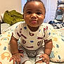 baby, child, cute, smiling, tongue_out, sitting, spiderman, clothing, pillow, pattern, indoor, blanket, bed, socks, person, face, curly_hair, happy, home, playful