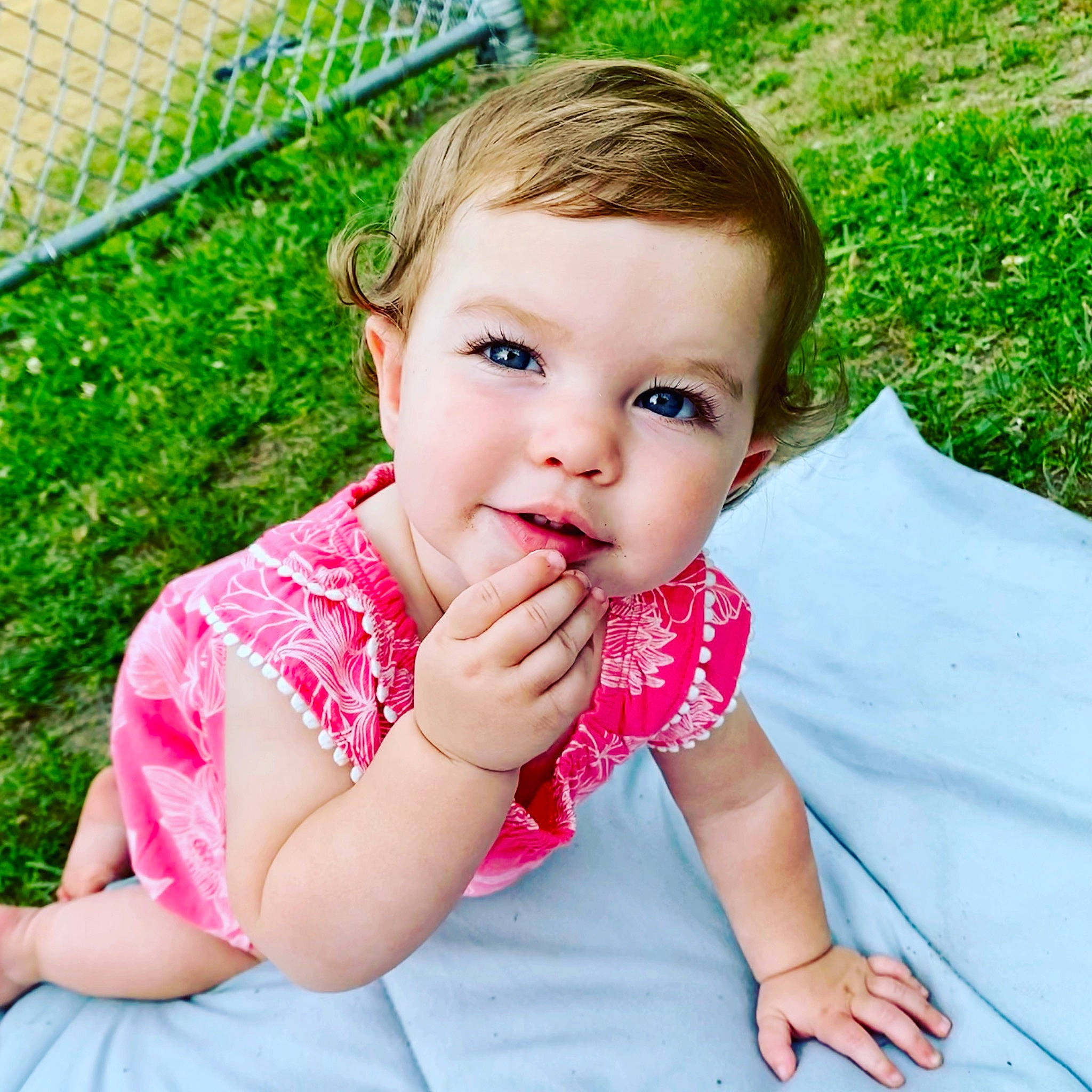 Aliza is registered to the contest to win money with this photo: arm, baby_toddler_clothing, cheek, clothing, dress, eyelash, finger, gesture, grass, happy, head, lip, nose, people_in_nature, person, pink, plant, product, skin, summer