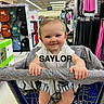 baby, backpacks, child, clothing, cute, foot, footwear, handle, happy, indoor, infant, person, rack, retail, retail_display, shopping_cart, shorts, smile, store, white_shirt