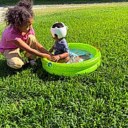 Douglas joined the competition — help win amazing prizes! child, children, outdoor, grass, inflatable_pool, water, helmet, playing, sitting, crouching, building, brick_wall, window, sunlight, daytime, greenery, holding_hands, protective_gear, young_child, older_child