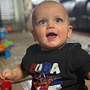 Axel is registered to the contest to win money with this photo: baby, blue_eyes, child, clothing, cute, expression, face, floor, furniture, happy, indoor, infant, mouth_open, person, portrait, short_hair, sitting, smiling, toy, tshirt