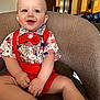 baby, child, smiling, red_bow_tie, red_suspender, shorts, shirt, indoor, chair, seated, happy, cute, portrait, blue_eyes, light_skin, hands, feet, furniture, casual_clothing, home