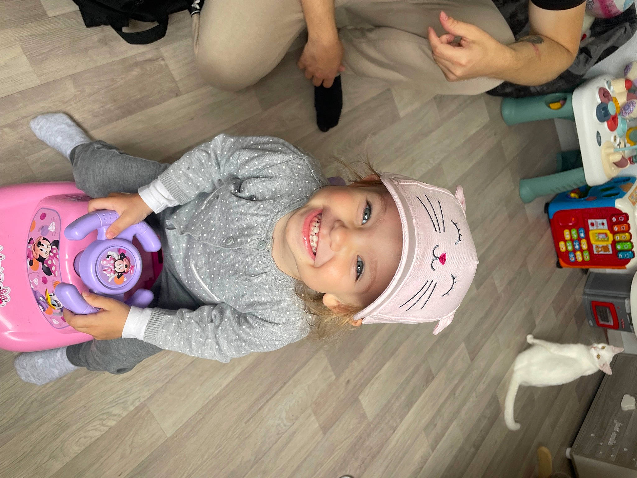 Gianna a rejoint le concours — aidez-le/la à gagner de superbes lots ! baby, baby_toddler_clothing, child, comfort, flooring, fun, happy, hardwood, headwear, joy, mouth, person, play, room, sitting, smile, t_shirt, toddler, varnish, white