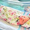 Genesis is registered to the contest to win money with this photo: newborn, baby, infant, sleeping, floral_blanket, headband, pearl_necklace, hospital_bassinet, soft_lighting, closeup, portrait, peaceful, cute, wrapped, child, human, resting, indoors, pink, white