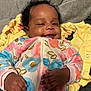 baby, blanket, child, comfort, cozy, curly_hair, cute, face, floral_pattern, hands, happy, indoor, infant, lying_down, onesie, portrait, smile, soft_texture, warm, yellow_clothing