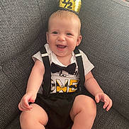 Tommy is registered to the contest to win money with this photo: baby, child, smiling, crown, gold, black_suspender, black_bow_tie, white_shirt, sitting, couch, gray_couch, happy, indoors, cute, portrait, infant, celebration, one_half, young_child, comfortable