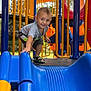 child, playground, slide, blue_slide, yellow_bars, orange_structure, smiling, short_hair, sandals, outdoor, daylight, metal_platform, clothing, happy, boy, play, fun, reaching, toy, park